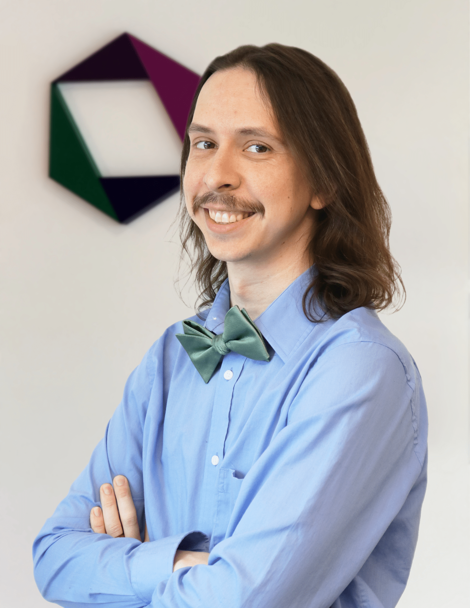 Ben Kass smiles at the camera while standing in front of the EK logo.